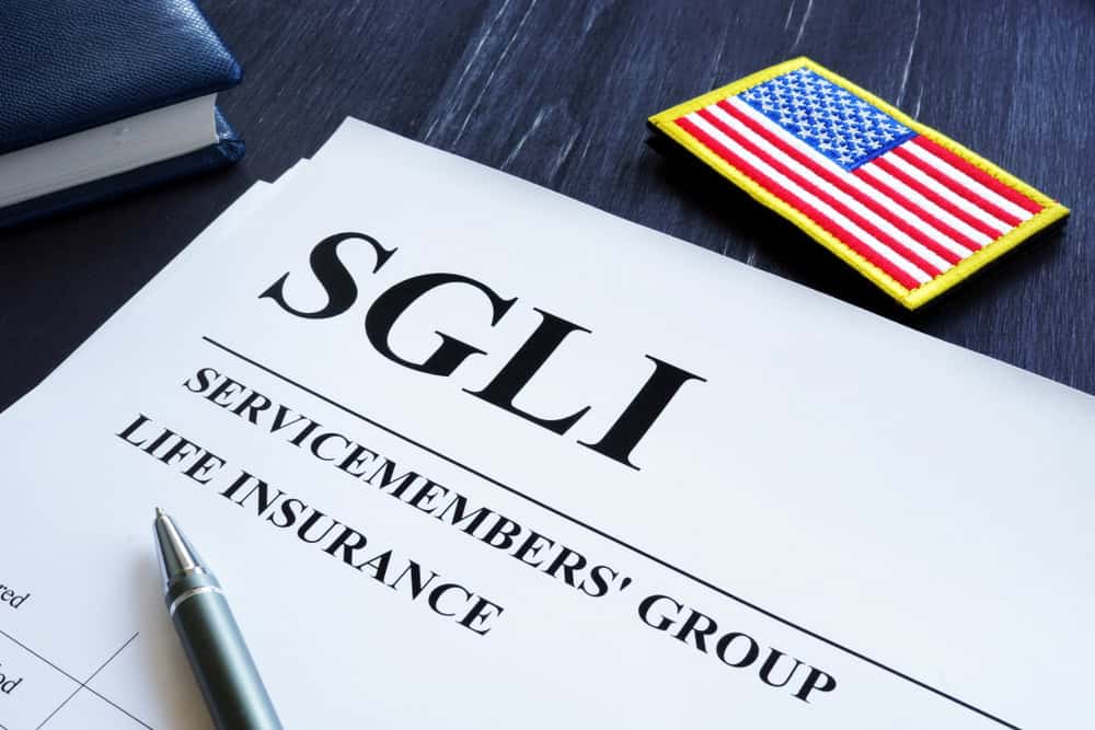 A document titled SGLI (Servicemembers' Group Life Insurance) on a desk, next to a pen, a book, and an American flag patch.
