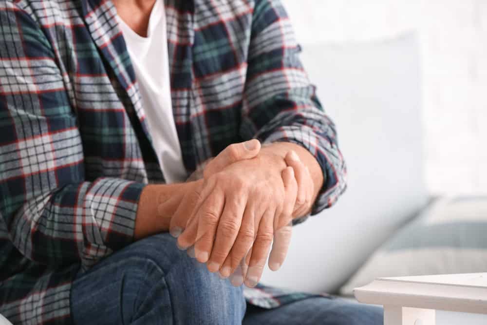 A person experiencing hand tremors while seated on a couch, illustrating symptoms considered in VA disability benefits for Parkinson’s disease.
