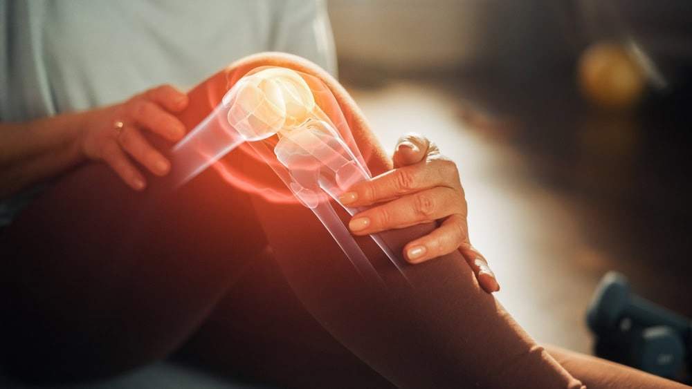 Person holding their knee with a digital graphic overlay showing joint pain and inflammation.