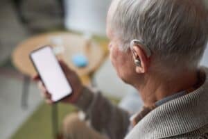 Older adult using a hearing aid while looking at a phone, illustrating VA hearing loss rating and hearing impairment evaluation.
