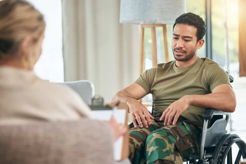 A veteran seated in a wheelchair speaking with a counselor, representing evaluation and support related to disability benefits.