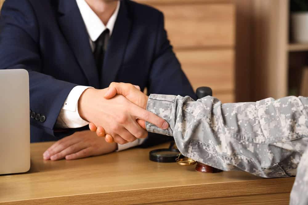A handshake between a person in a suit (like a lawyer or professional) and a person in a military camouflage uniform.