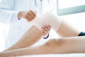 Doctor wrapping a patient’s injured knee with a compression bandage during a medical examination.