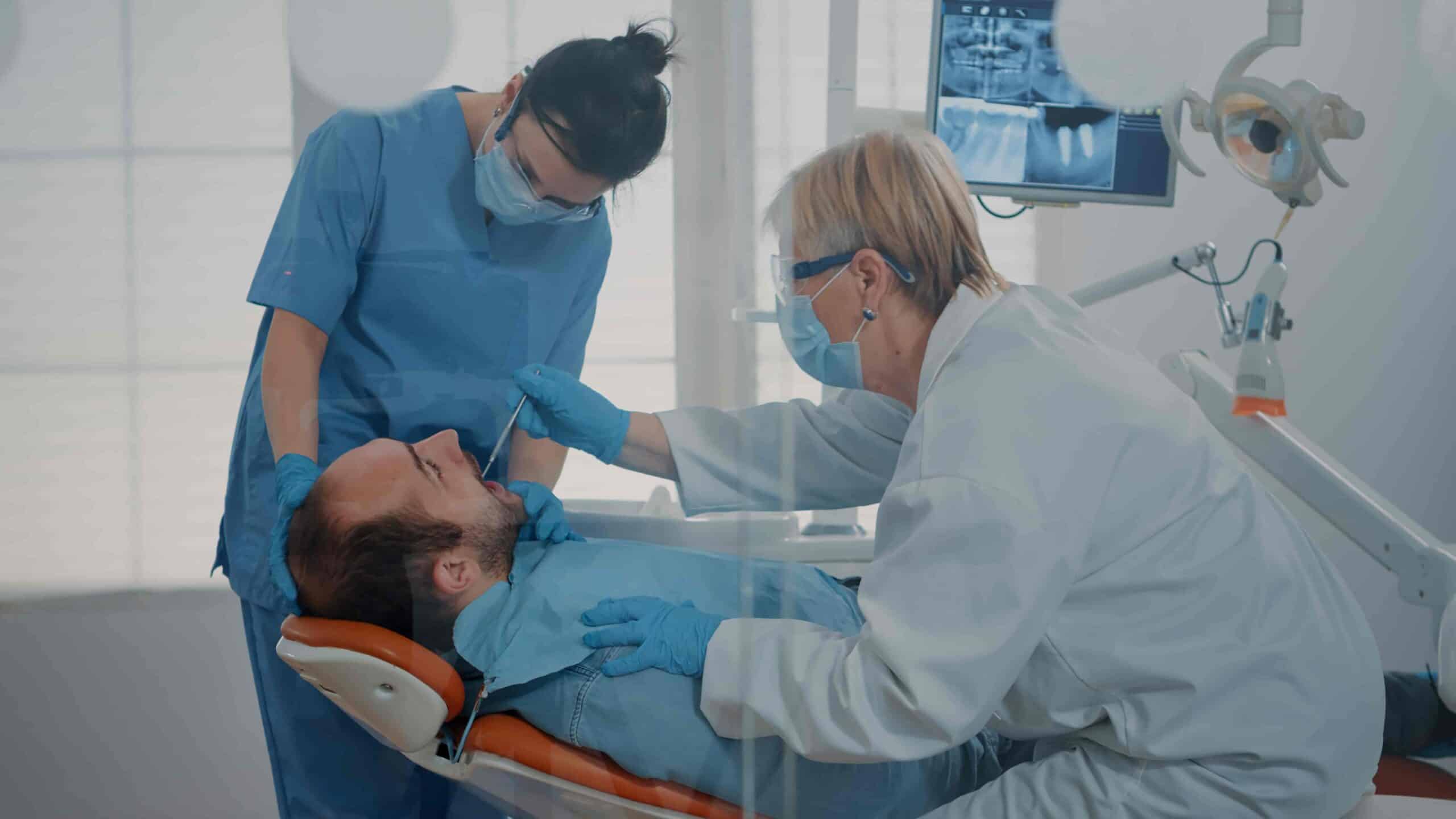 Dentist and assistant performing dental examination on patient in clinic to assess eligibility for VA dental care services